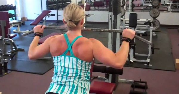 Tração vertical da máquina de exercício. Técnica para sentar, de costas, atrás da cabeça, com pegada estreita para mulheres